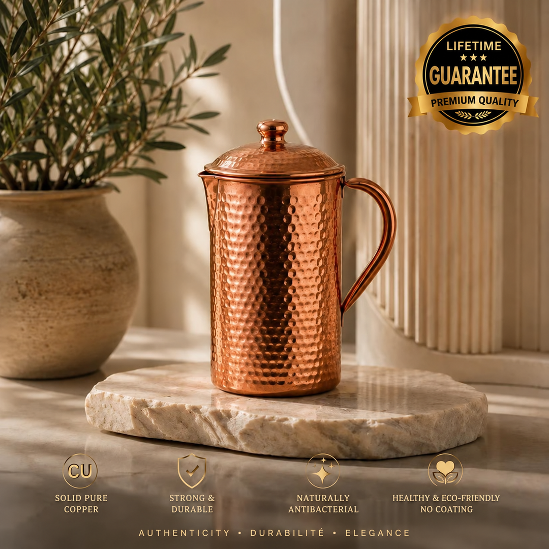 Hammered copper water carafe with lid and handle on a marble slab, styled with a potted plant