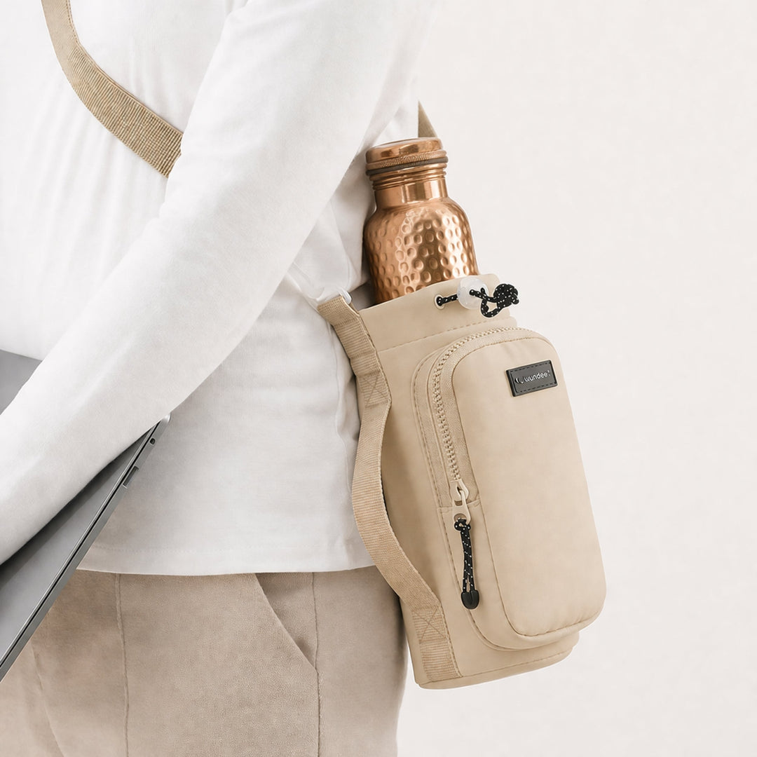 Beige crossbody carrier bag worn on the hip with a copper water bottle held inside the top pocket
