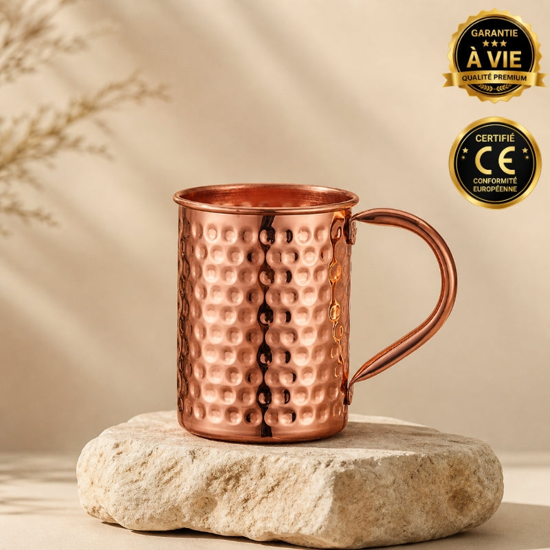 Hammered copper Moscow mule mug with angled handle, displayed on a stone base