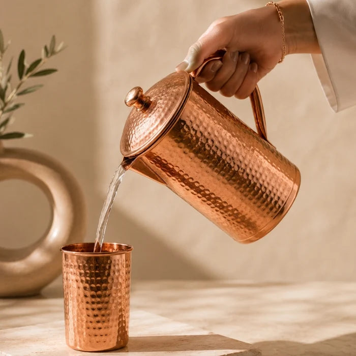 Hammered copper carafe with 2 matching copper cups displayed as a set